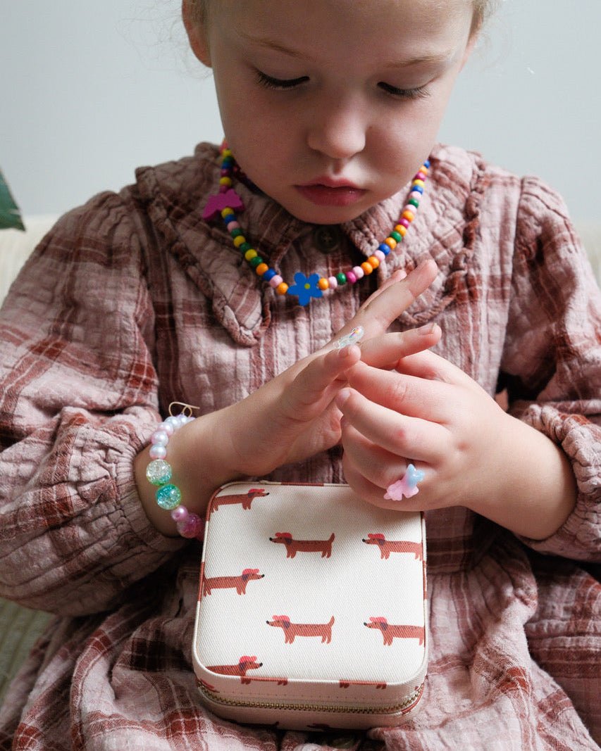 Enfant avec des bijoux qui met des bagues avec une boite à bijou à motif chien sur les genoux