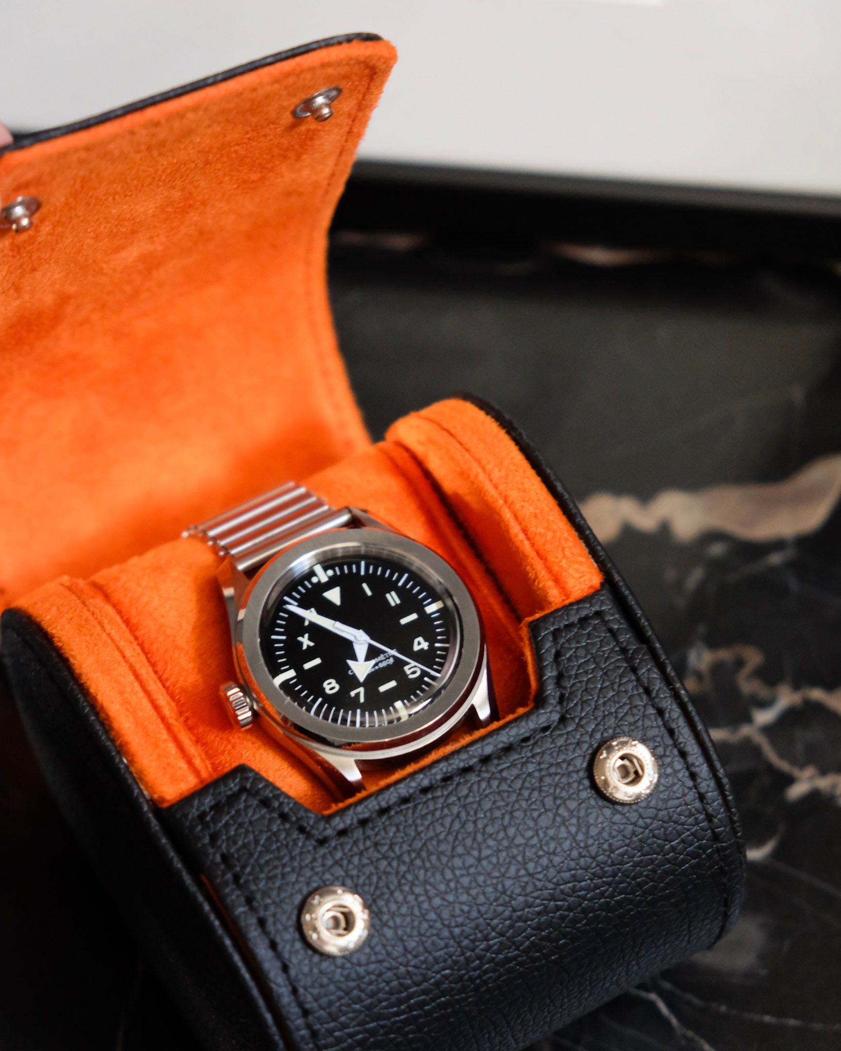 boite à montre ouverte extérieur cuir noir et intérieur velours orange avec une montre à l'intérieur
