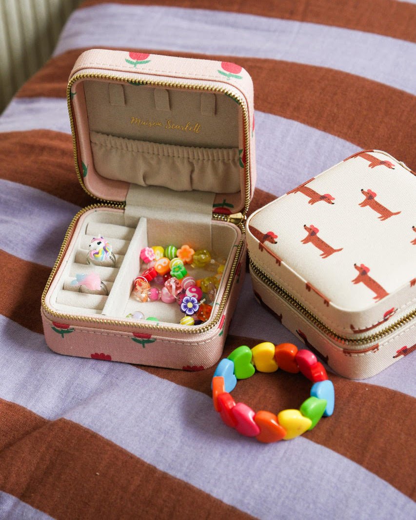 une boite à bijou motifs fleurs ouverte avec des bijoux fantaisie et une boite à bijou motif chien sur fond rayé